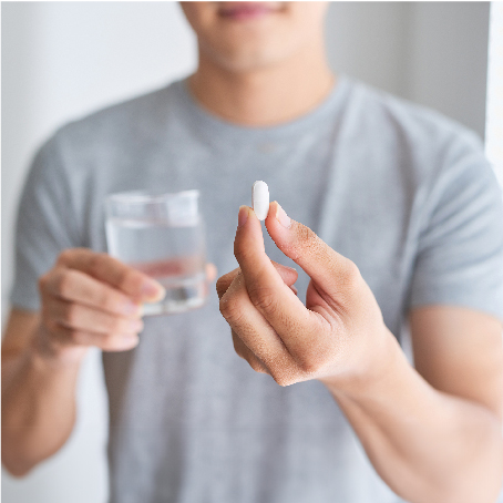 A man holding a cup of water in one hand and a pill in the other hand