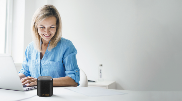 A woman at office desk using computer, talking to iFORA IntelliSpeaker