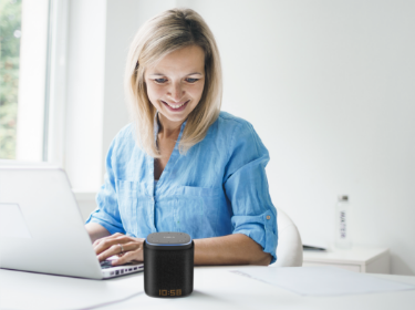 A woman at office desk using computer, talking to iFORA IntelliSpeaker