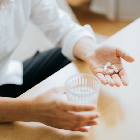 A man at a table with a water cup in one hand and nutritional supplements in the other