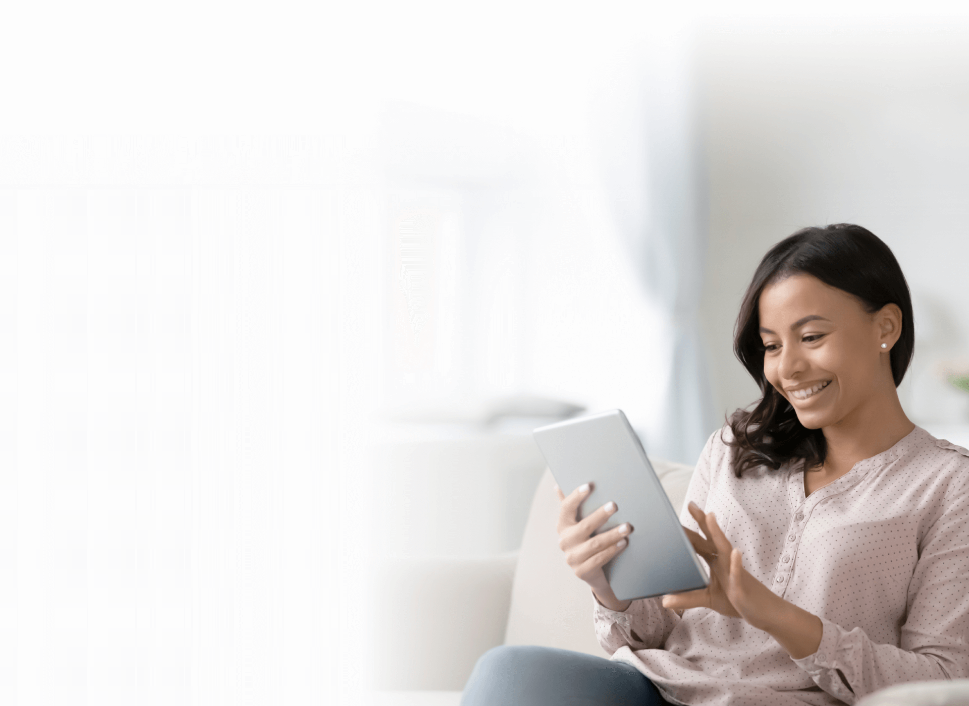 A woman sitting on the sofa, joyfully using a tablet