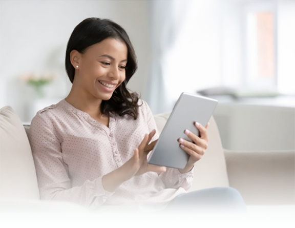 A smiling woman sitting on the sofa at home, using a tablet