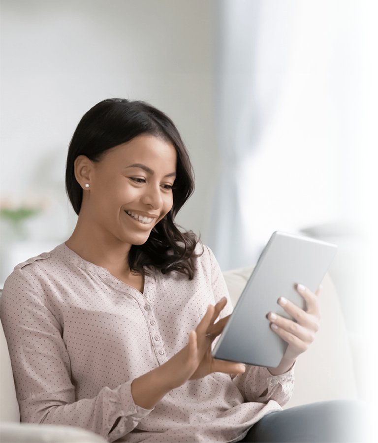 A smiling woman sitting on the sofa at home, using a tablet