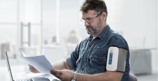 Middle-aged man at desk, checking blood pressure level with FORA TN'G BP