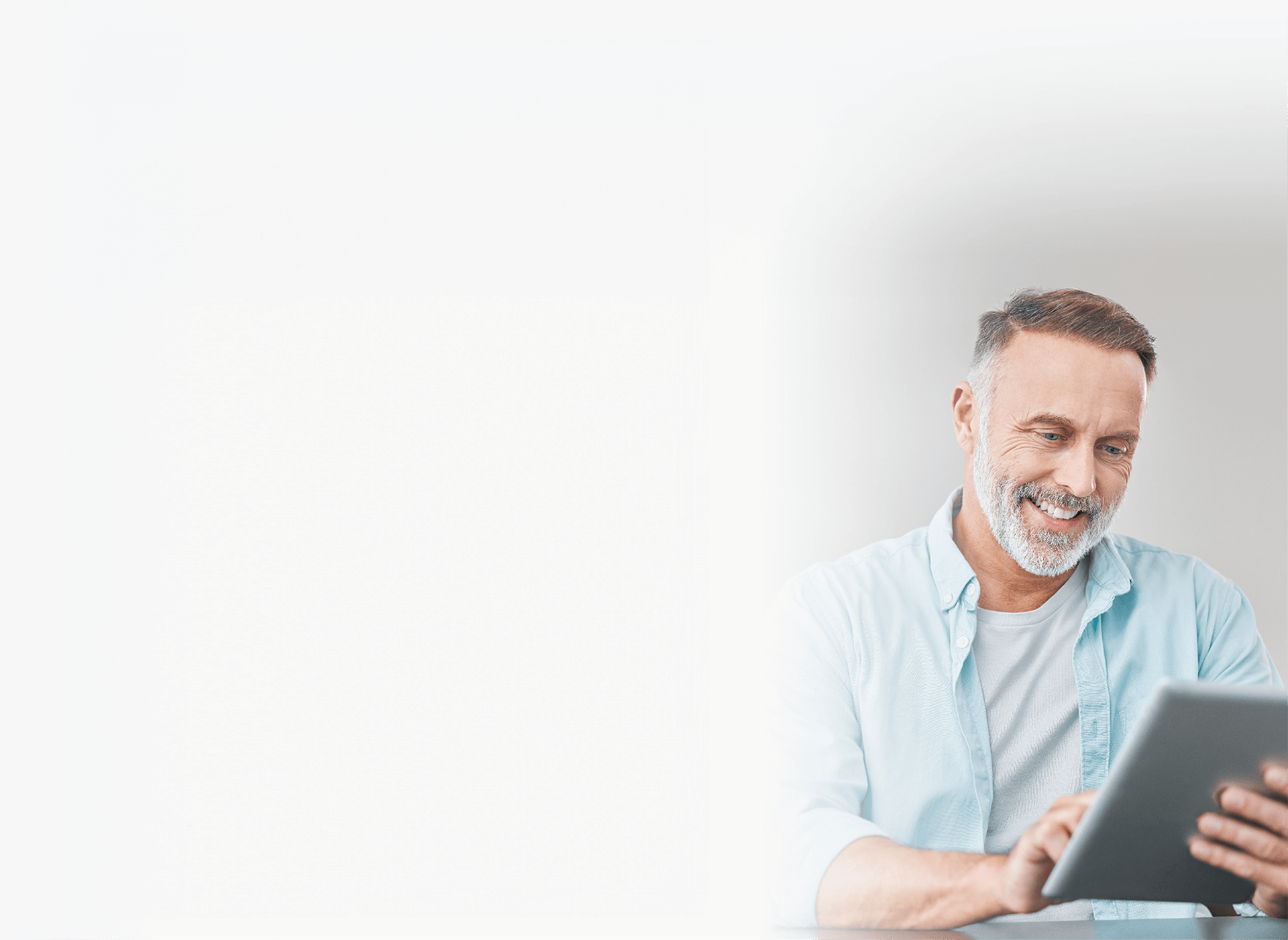 A middle-aged man sits at a table using a tablet