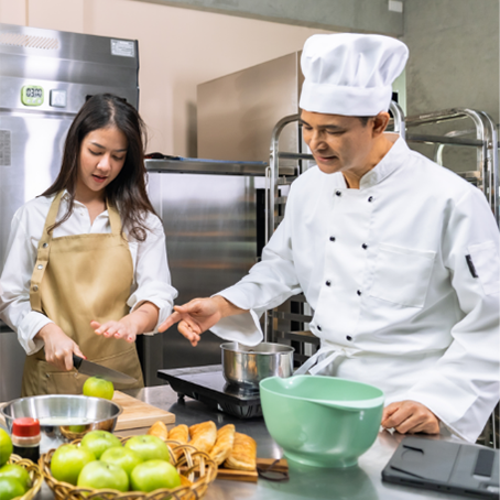 A chef teaching a student how to cut an apple, preparing to make desserts